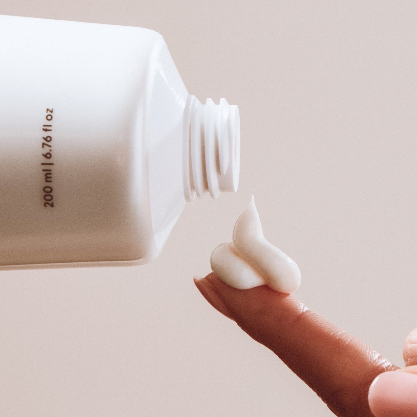 Hand holding a small amount of white conditioner next to a larger white container.