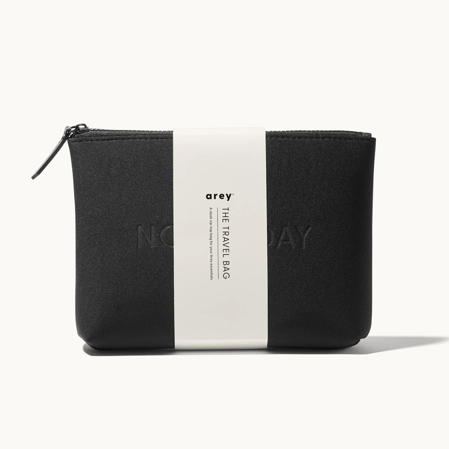 Arey "Not Today" black travel bag with a white paper band wrapped around it. The band reads: arey. THE TRAVEL BAG. A sleek zip-top bag for your Arey essentials.