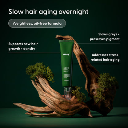 A green tube of Arey The Beauty Sleep Duo stands between two pieces of driftwood on a dark green background, with text highlighting benefits like slowing greys, supporting new hair growth, and promoting overall hair wellness.