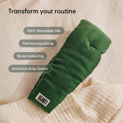 A padded sleep mask from Arey’s Beauty Sleep Duo in the exclusive Arey Green shade, labeled LUNI, rests on a beige quilt. Made from 100% washable silk, this thermoregulating and noise-reducing mask is designed to enhance your nightly hair wellness routine.