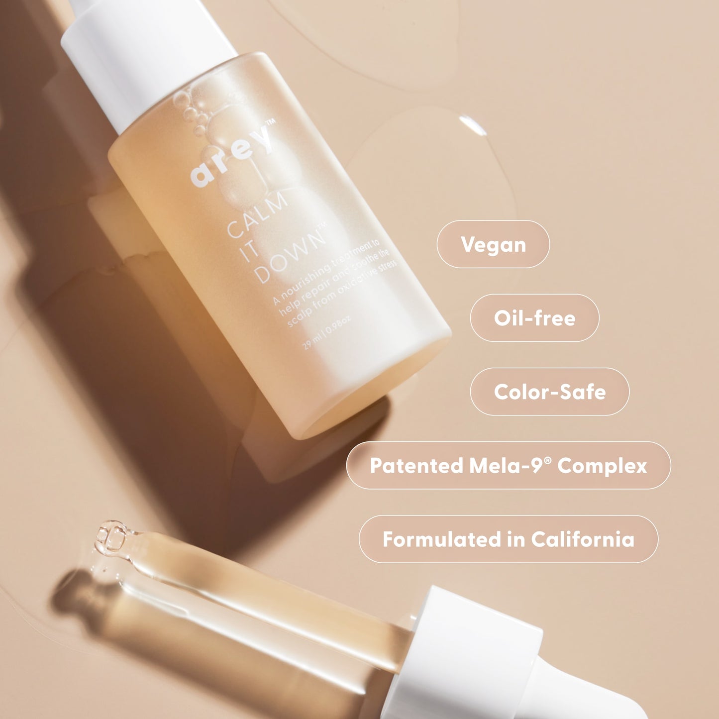 A dropper bottle labeled Arey Calm It Down Scalp Serum rests on a beige surface with drops of skincare liquid, offering the perfect solution to soothe and protect your scalp. Text highlights: Vegan, Oil-free, Color-Safe, Patented Mela-9 Complex, Formulated in California.