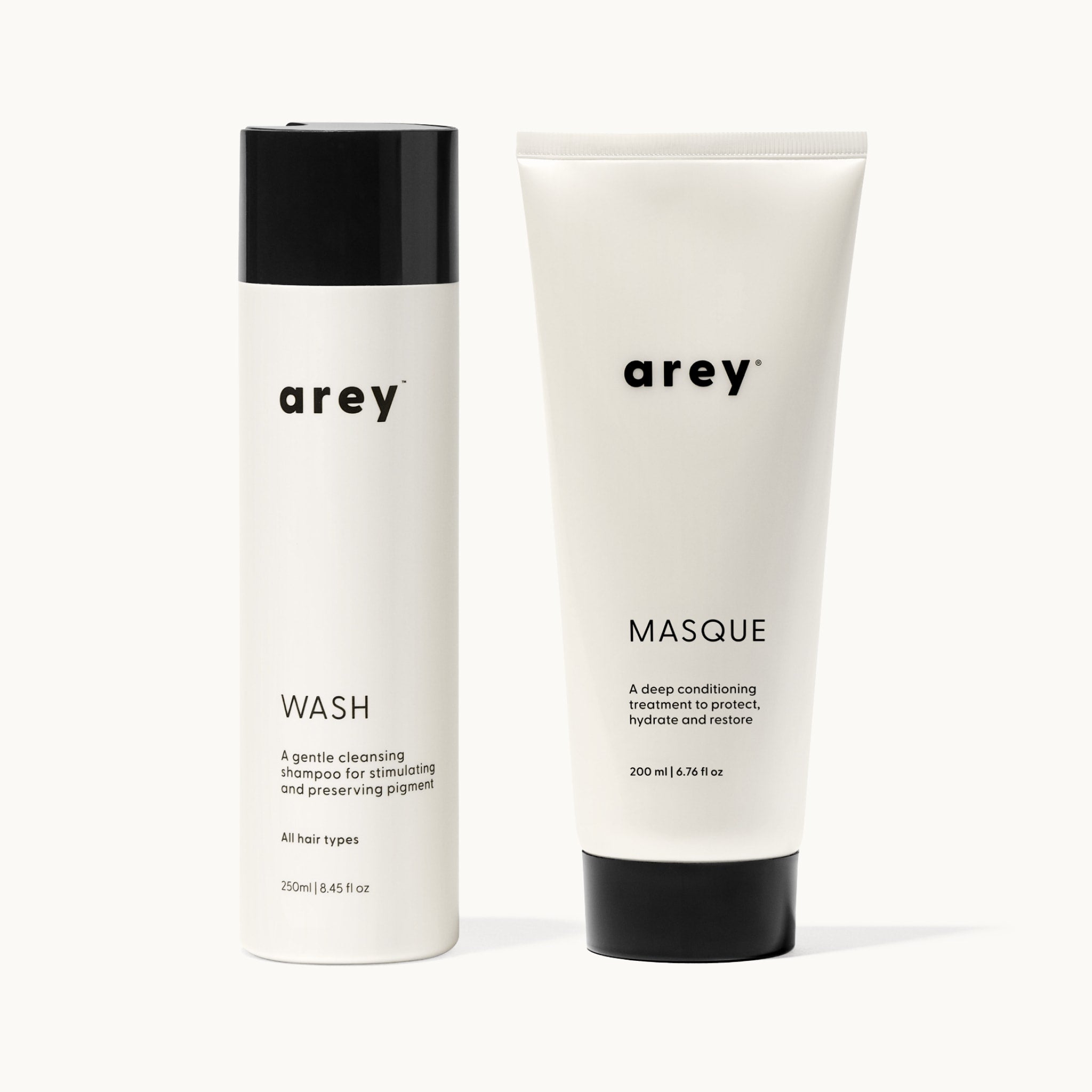 Lineup product photo of the Arey Deep Treatment Duo on a cream background. Left: Wash shampoo bottle (250ml) — a gentle cleansing shampoo for stimulating and preserving pigment, all hair types. Right: Masque tube (200ml) — a deep conditioning treatment to protect, hydrate and restore.