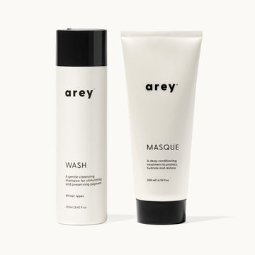Lineup product photo of the Arey Deep Treatment Duo on a cream background. Left: Wash shampoo bottle (250ml) — a gentle cleansing shampoo for stimulating and preserving pigment, all hair types. Right: Masque tube (200ml) — a deep conditioning treatment to protect, hydrate and restore.