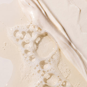 Close-up of soap bubbles and creamy white liquid spread across a smooth surface, forming a textured and abstract pattern—evoking the rich nourishment of Arey’s The Deep Treatment Duo, an ideal choice for those looking for an effective deep conditioner designed to help delay greys.