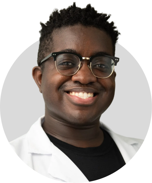 A person wearing glasses and a white lab coat smiles at the camera against a light gray background.