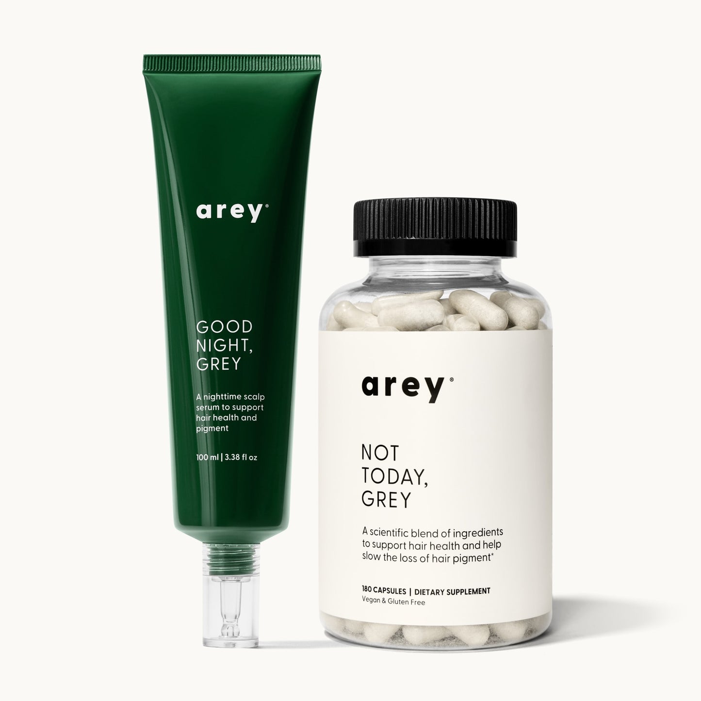 Arey Dream Duo product shot. Left: dark green tube labeled "arey / GOOD NIGHT, GREY / A nighttime scalp serum to support hair health and pigment / 100 ml | 3.38 fl oz." Right: clear bottle with black lid labeled "arey / NOT TODAY, GREY / Physician-formulated to slow the loss of hair pigment and support hair health* / 180 CAPSULES | DIETARY SUPPLEMENT / Vegan & Gluten Free."