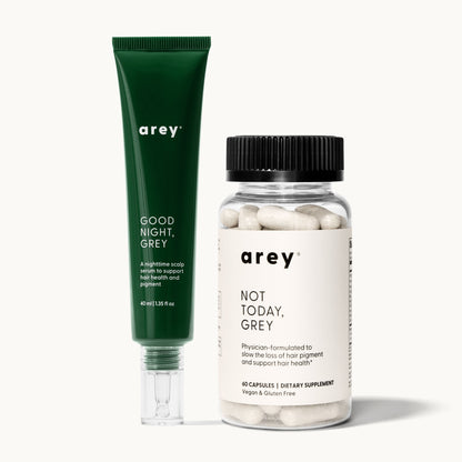 Arey Dream Duo product shot. Left: dark green tube labeled "arey / GOOD NIGHT, GREY / A nighttime scalp serum to support hair health and pigment / 40 ml | 1.35 fl oz." Right: clear bottle with black lid labeled "arey / NOT TODAY, GREY / Physician-formulated to slow the loss of hair pigment and support hair health* / 60 CAPSULES | DIETARY SUPPLEMENT / Vegan & Gluten Free."