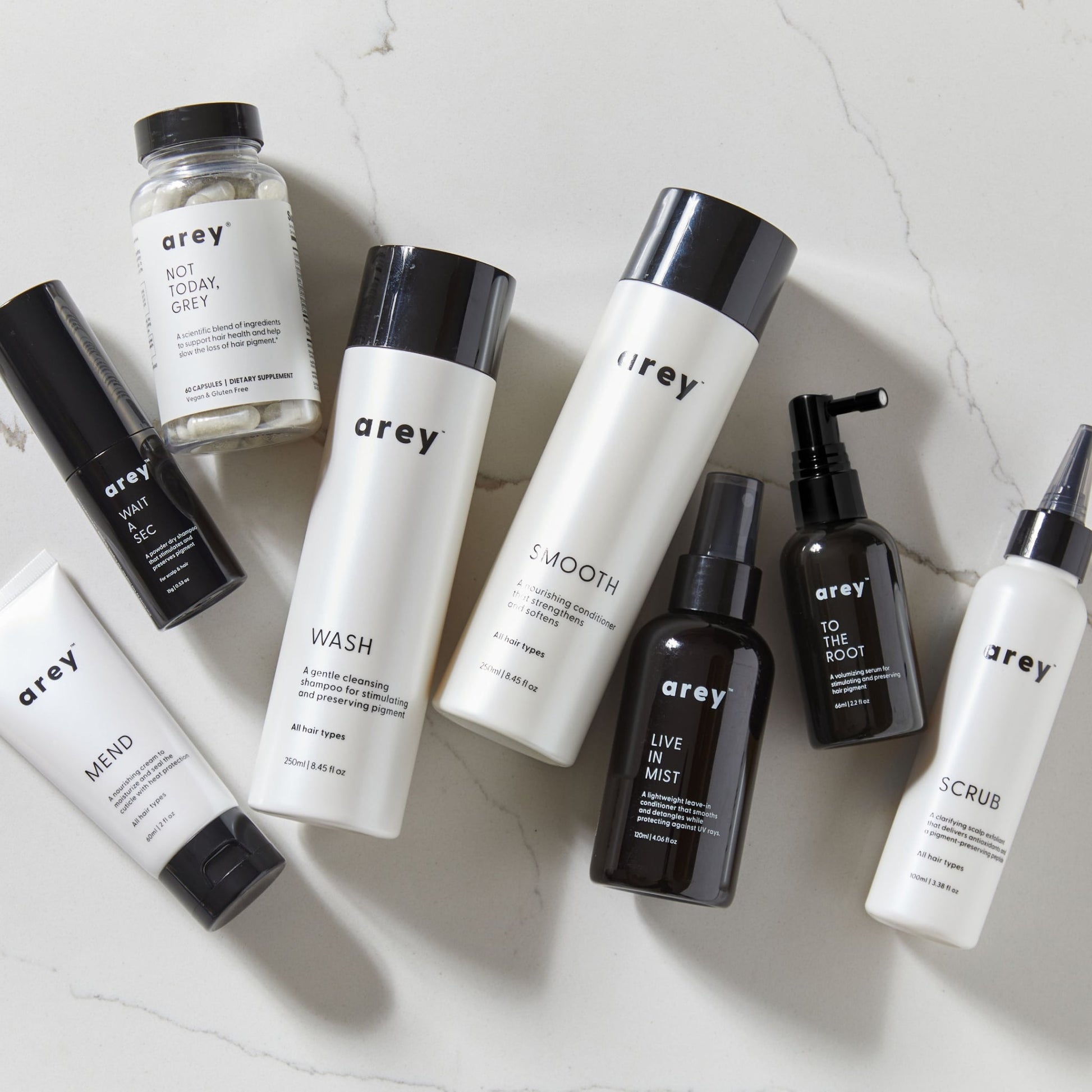 Group of products resting on marble tile. Products include Mend, Wait A Sec, Not Today Grey, Wash Shampoo, Smooth Conditioner, Live In Mist, To The Root, and Scrub