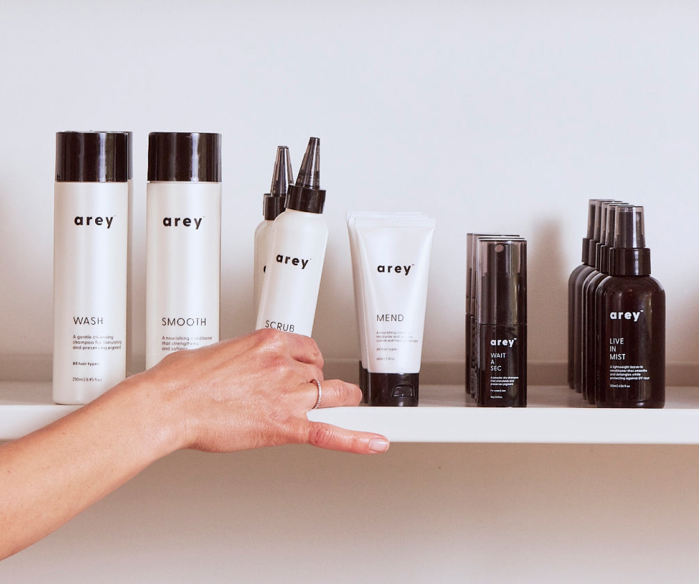 Persons hand grabbing Scrub off of a shelf of Arey products 