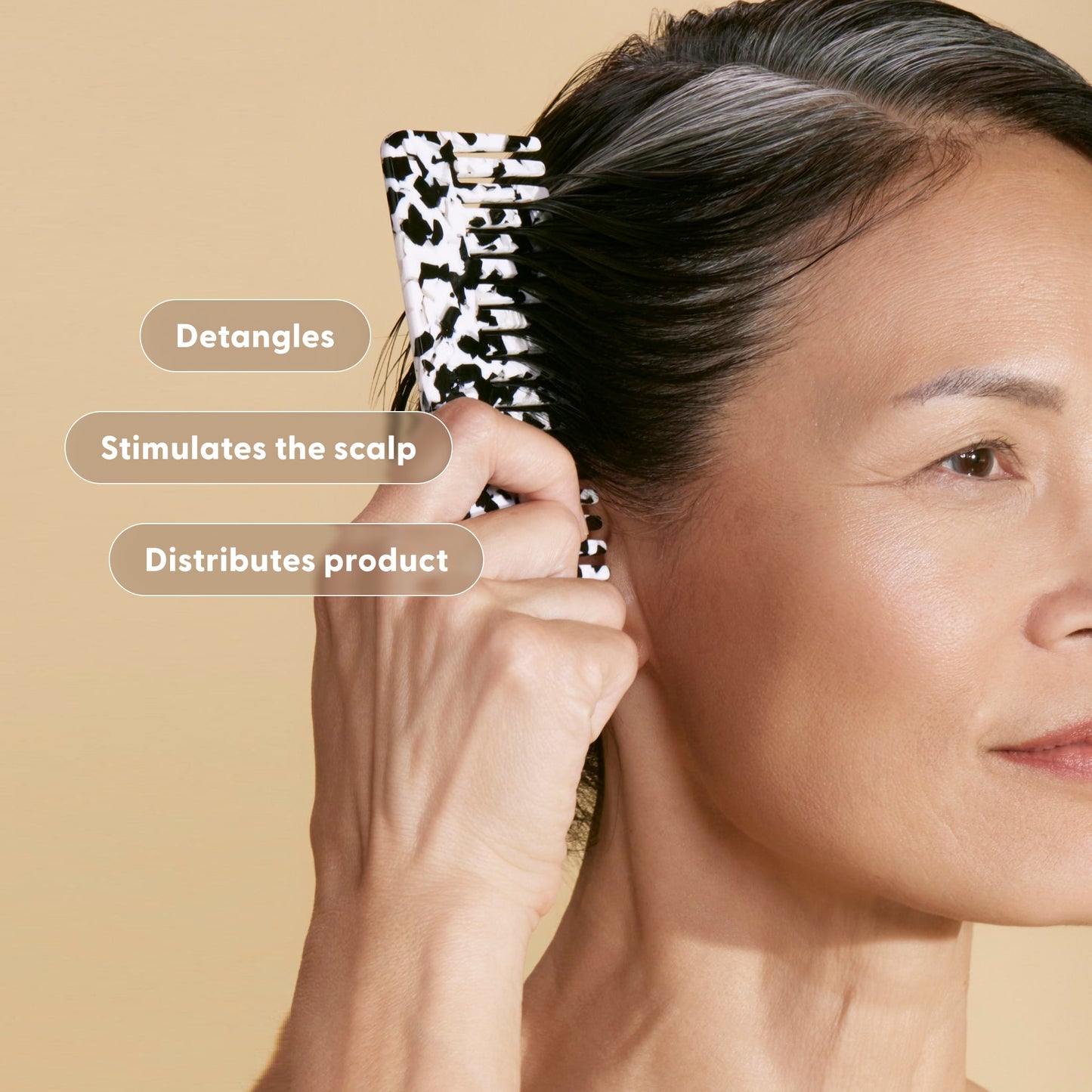 Lifestyle photo of a woman combing her hair with an arey black and white patterned hair comb against a warm tan background. Feature badges overlay the image: Detangles, Stimulates the scalp, Distributes product.