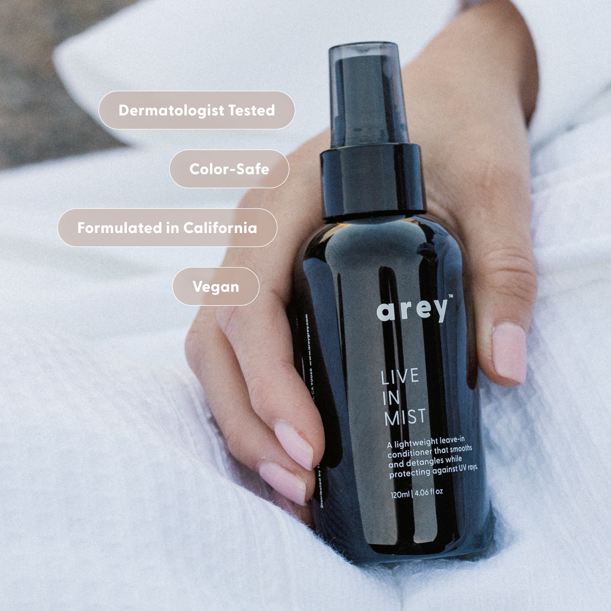 Hand holding a black spray bottle labeled 'arey' with product features listed above.