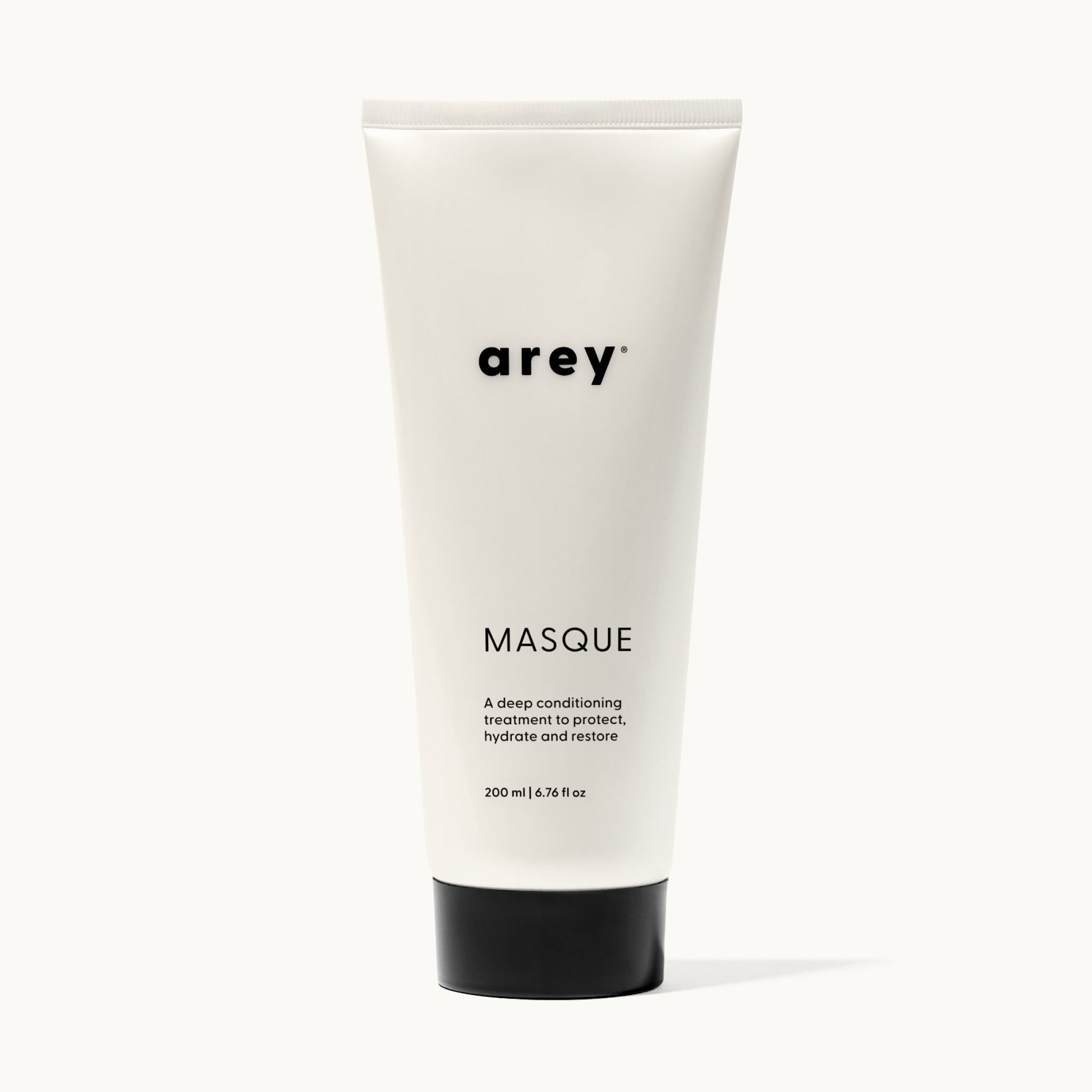 Product shot of arey Masque tube on a white/cream background. Label reads: arey® MASQUE. "A deep conditioning treatment to protect, hydrate and restore." 200 ml | 6.76 fl oz.