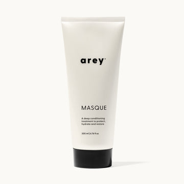 Product shot of arey Masque tube on a white/cream background. Label reads: arey® MASQUE. "A deep conditioning treatment to protect, hydrate and restore." 200 ml | 6.76 fl oz.