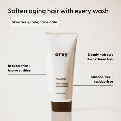 A white tube labeled Arey Masque Deep Conditioner stands upright, with surrounding text highlighting its hair benefits: repairs damaged hair, improves shine, deeply hydrates with a silicone-free formula, leaves no residue, features skincare-grade ingredients, and is color-safe.