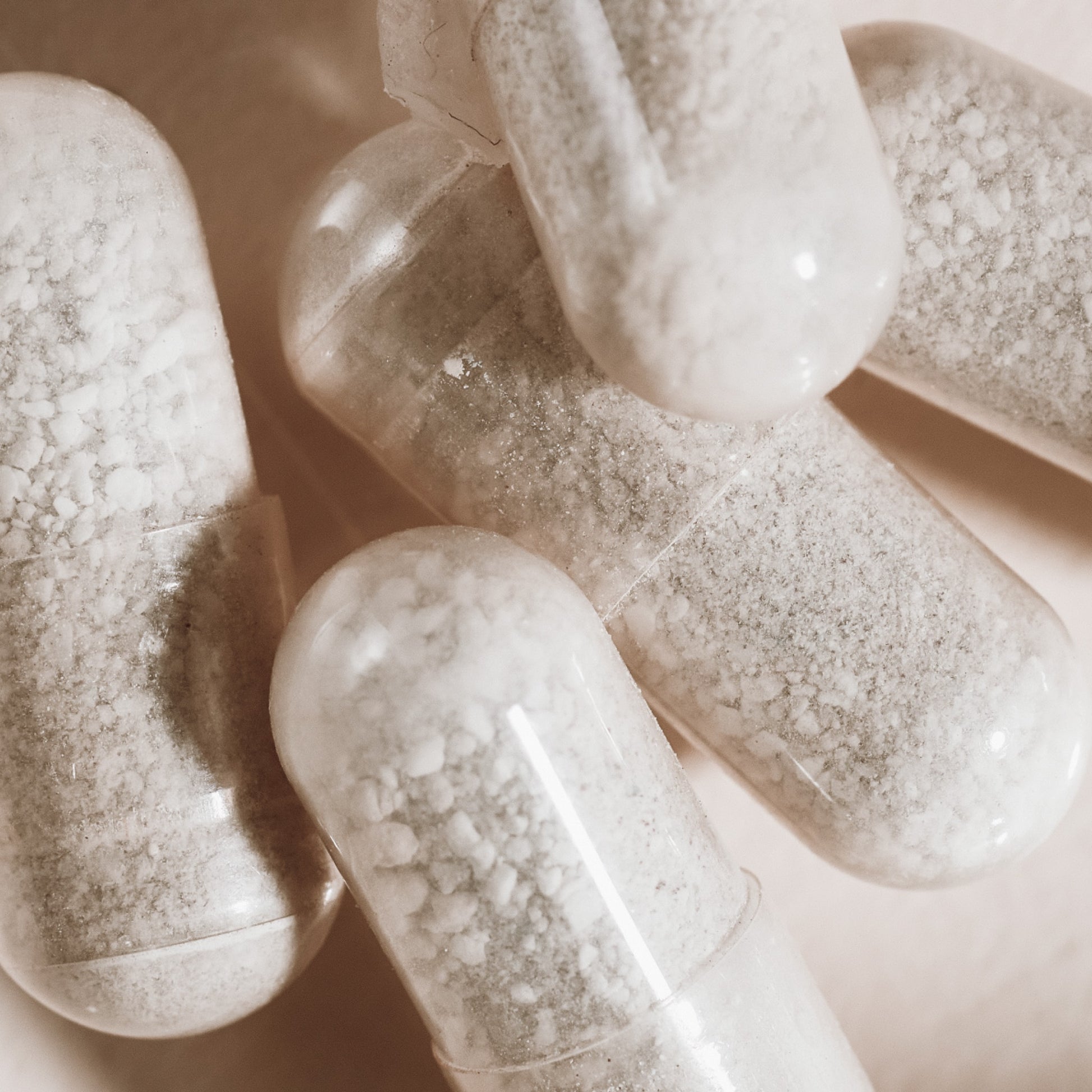Close-up of several clear capsules filled with coarse white powder, scattered on a light surface—these are Arey’s Not Today, Grey™ supplements, formulated to support hair repigmentation and promote thicker hair.