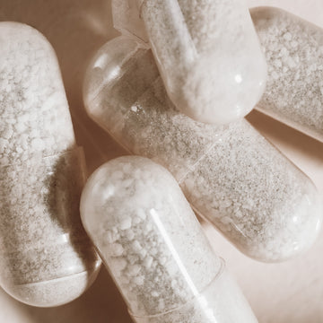 Close-up of several clear capsules filled with coarse white powder, scattered on a light surface—these are Arey’s Not Today, Grey™ supplements, formulated to support hair repigmentation and promote thicker hair.