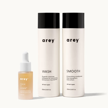 Three arey hair care products, Calm It Down, Wash, and Smooth on a white background