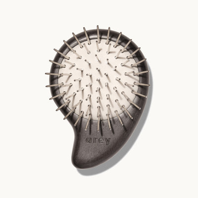 Arey Scalp Brush on cream background showing the bristle side. The dark wood brush has metal nickel-plated bristles on a natural rubber cushion base, with the arey brand name on the handle.