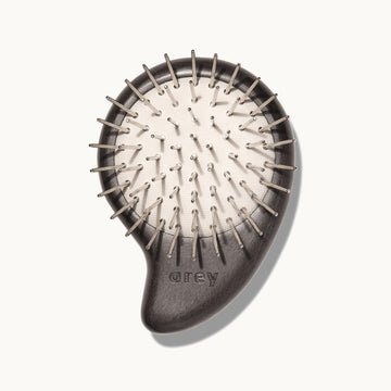 Arey Scalp Brush on cream background showing the bristle side. The dark wood brush has metal nickel-plated bristles on a natural rubber cushion base, with the arey brand name on the handle.