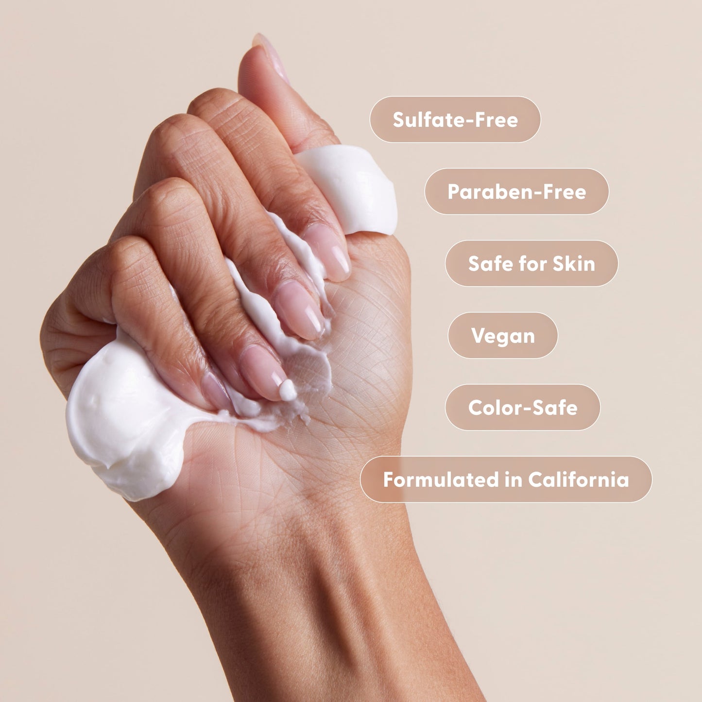 A hand squeezes white cream labeled: Sulfate-Free, Paraben-Free, Safe for Skin, Vegan, Color-Safe, Formulated in California. The light beige background is perfect for showcasing Arey’s The Shower Duo Refill and other in-shower care essentials.