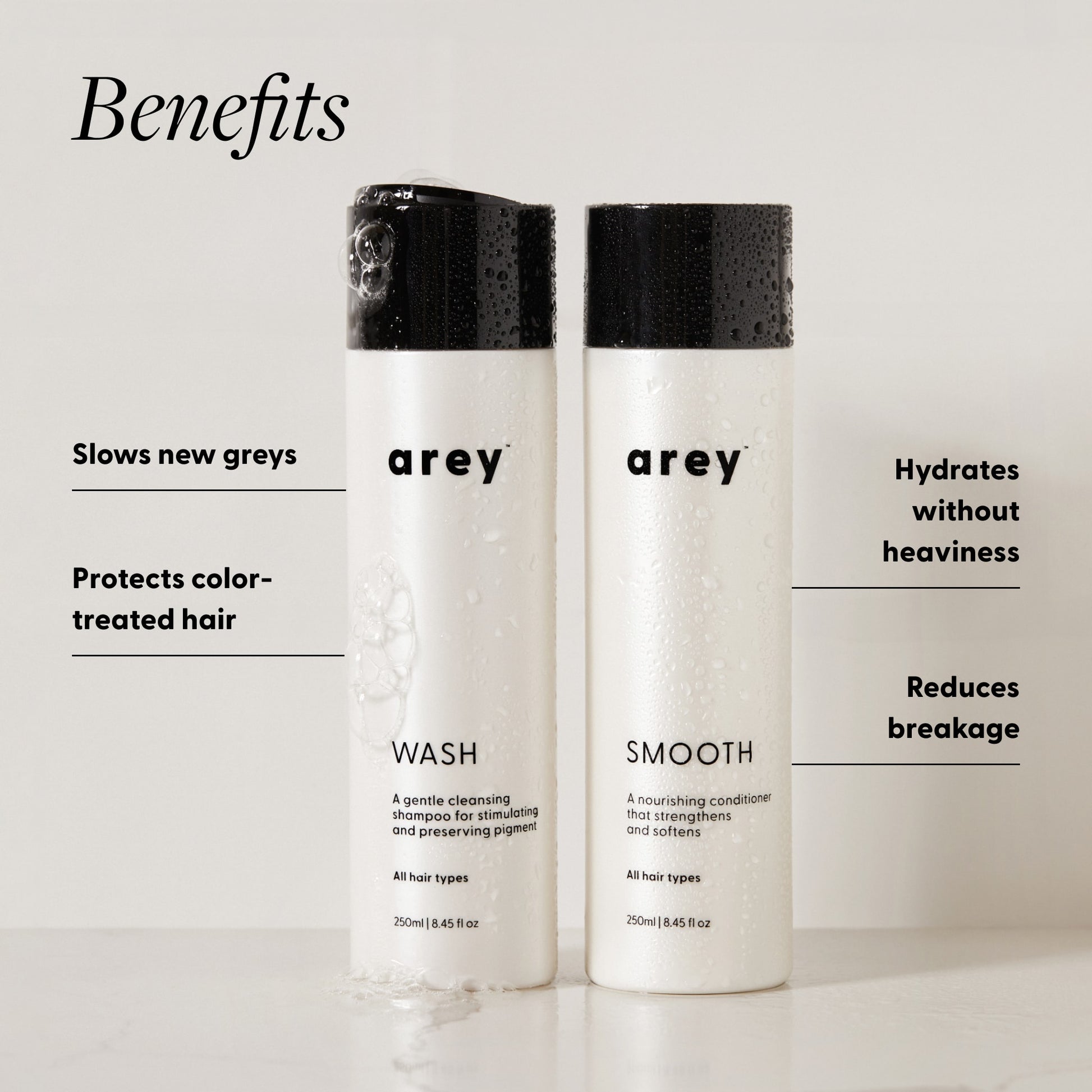 Arey Shower Duo Wash and Smooth bottles (250ml each) with benefits labeled. Text reads: Benefits — Slows new greys. Protects color-treated hair. Hydrates without heaviness. Reduces breakage.