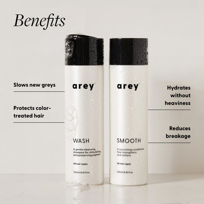 Arey Shower Duo Wash and Smooth bottles (250ml each) with benefits labeled. Text reads: Benefits — Slows new greys. Protects color-treated hair. Hydrates without heaviness. Reduces breakage.