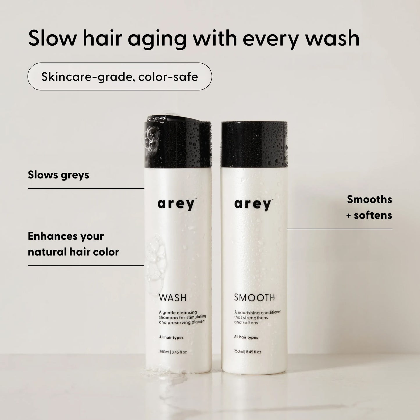 Two Arey The Shower Duo bottles labeled Wash and Smooth stand on a white surface. Text highlights the benefits: slows greys, enhances your natural hair color, and smooths + softens for healthier, more vibrant hair. Experience in-shower care from Arey that cleanses and restores your hair’s natural radiance.
