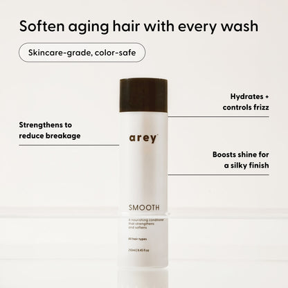 A white bottle of Arey Smooth Conditioner, topped with a black cap, is displayed against a light background. The text showcases its benefits: strengthening hair, providing hydration, controlling frizz, and enhancing shine. This nourishing Arey Smooth Conditioner offers a color-safe, skincare-grade formula created for smooth results and healthy hair.