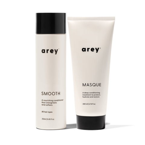 Two white bottles of Arey hair products: one labeled SMOOTH (conditioner) and the other MASQUE (deep conditioner), both with black caps, standing side by side on a light background.