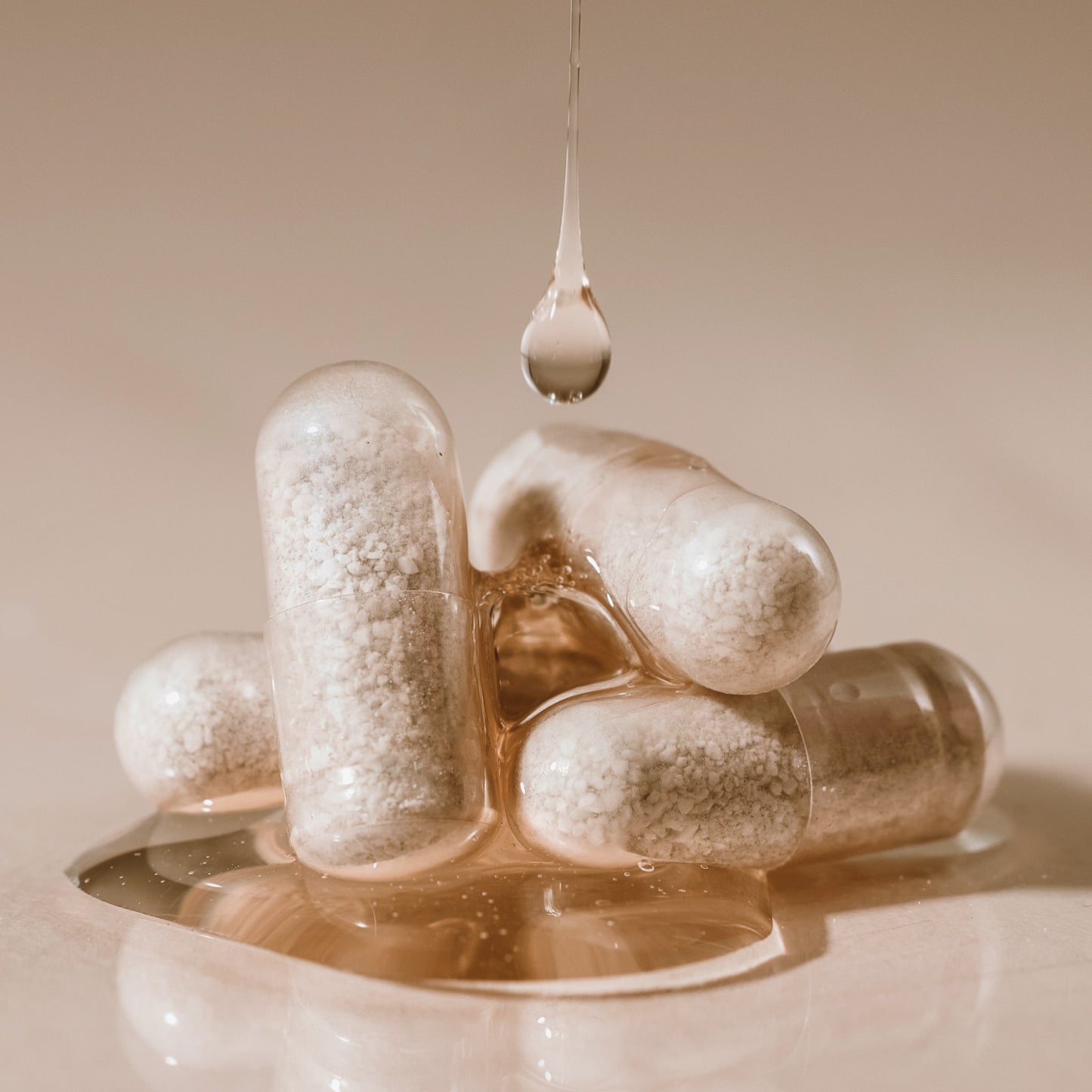 Close-up of Arey Not Today, Grey supplement capsules with a water droplet falling onto them, on a cream background.