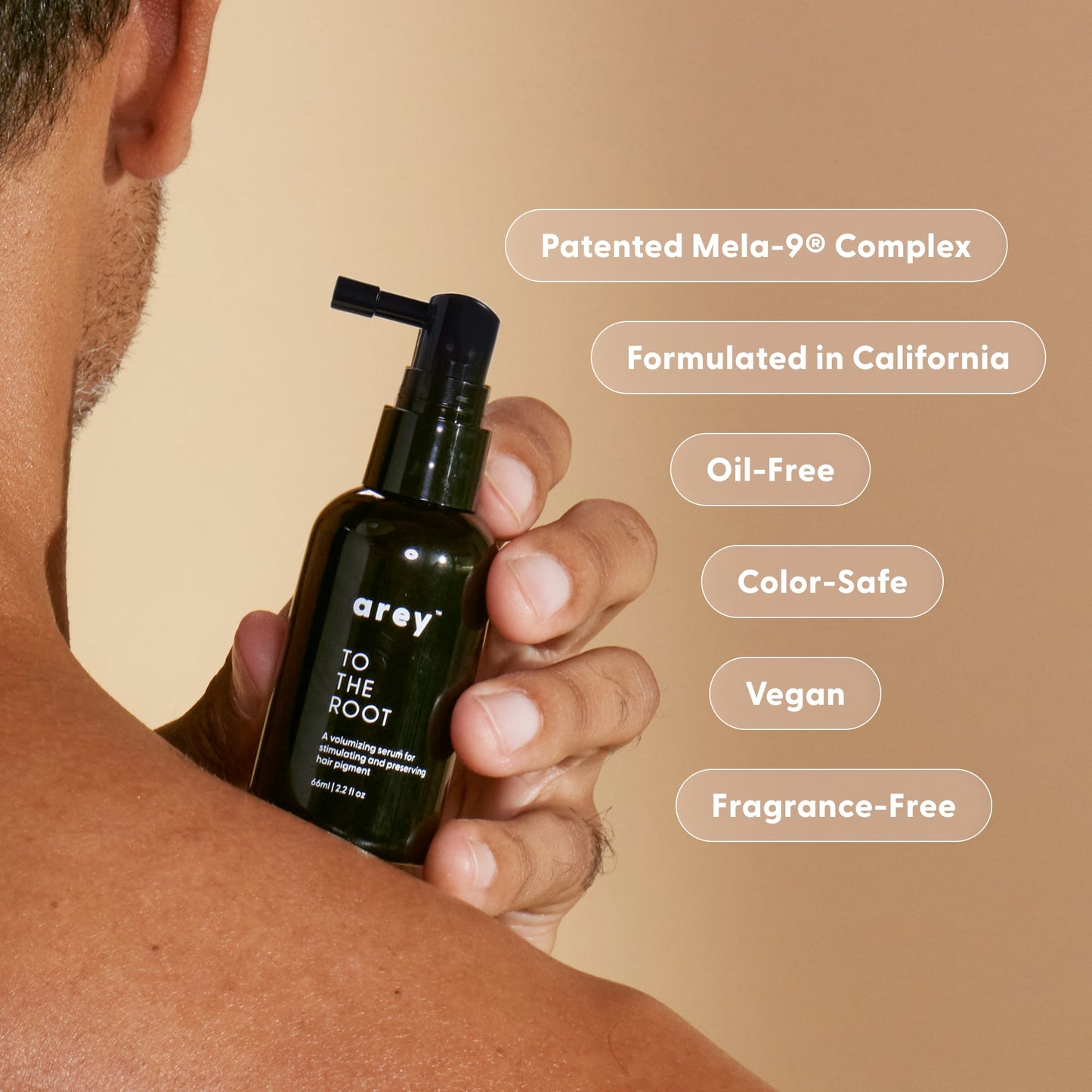 A person holds a green bottle of Arey To The Root® Scalp Serum, a treatment formulated to repigment grey hair and support the needs of aging hair. Text on the image highlights features: Patented Mela-9® Complex, Formulated in California, Oil-Free, Color-Safe, Vegan, and Fragrance-Free.
