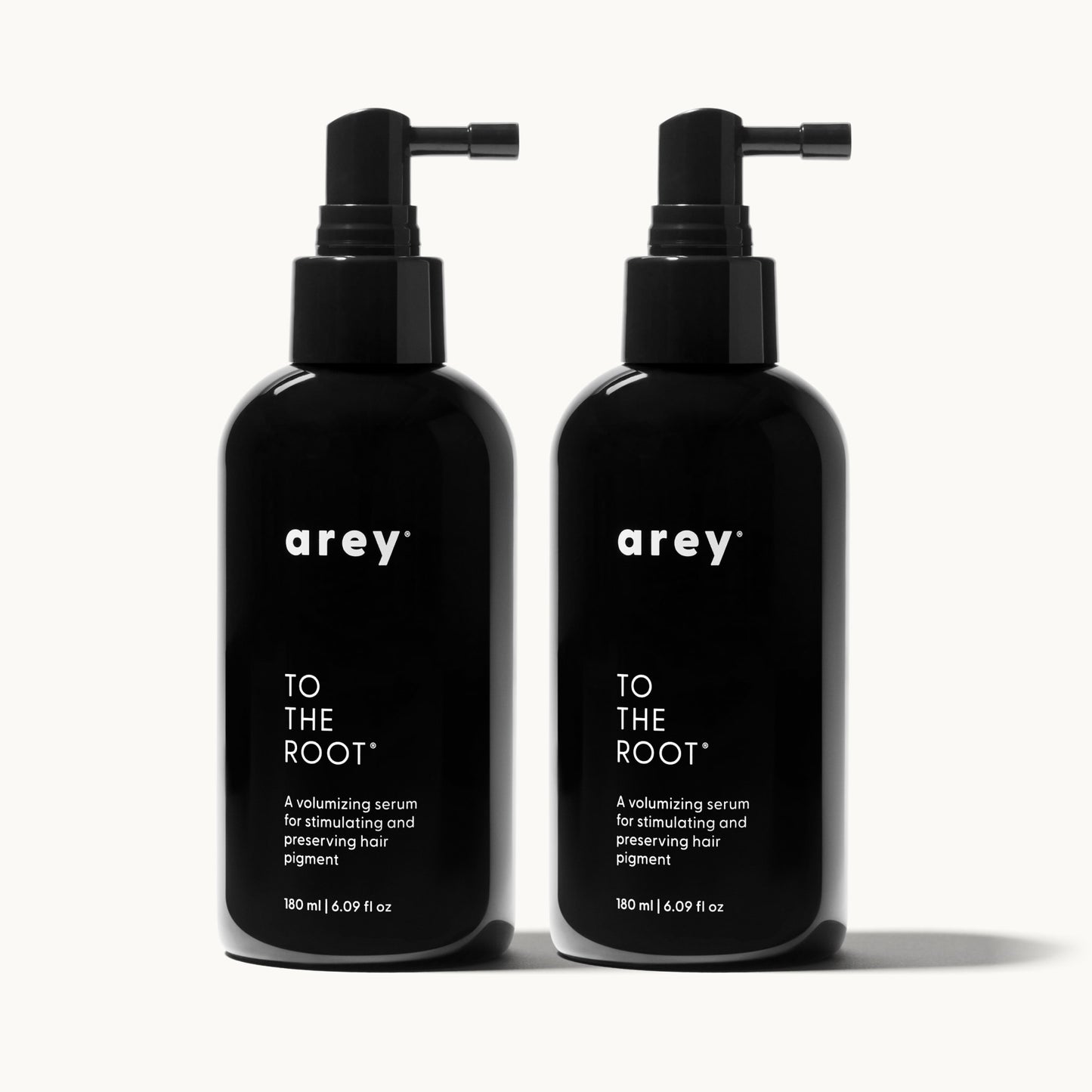 Two Arey To The Root serum bottles on a cream background, representing a 6-month supply. Both bottles labeled: arey. TO THE ROOT. A volumizing serum for stimulating and preserving hair pigment. 180 ml / 6.09 fl oz.
