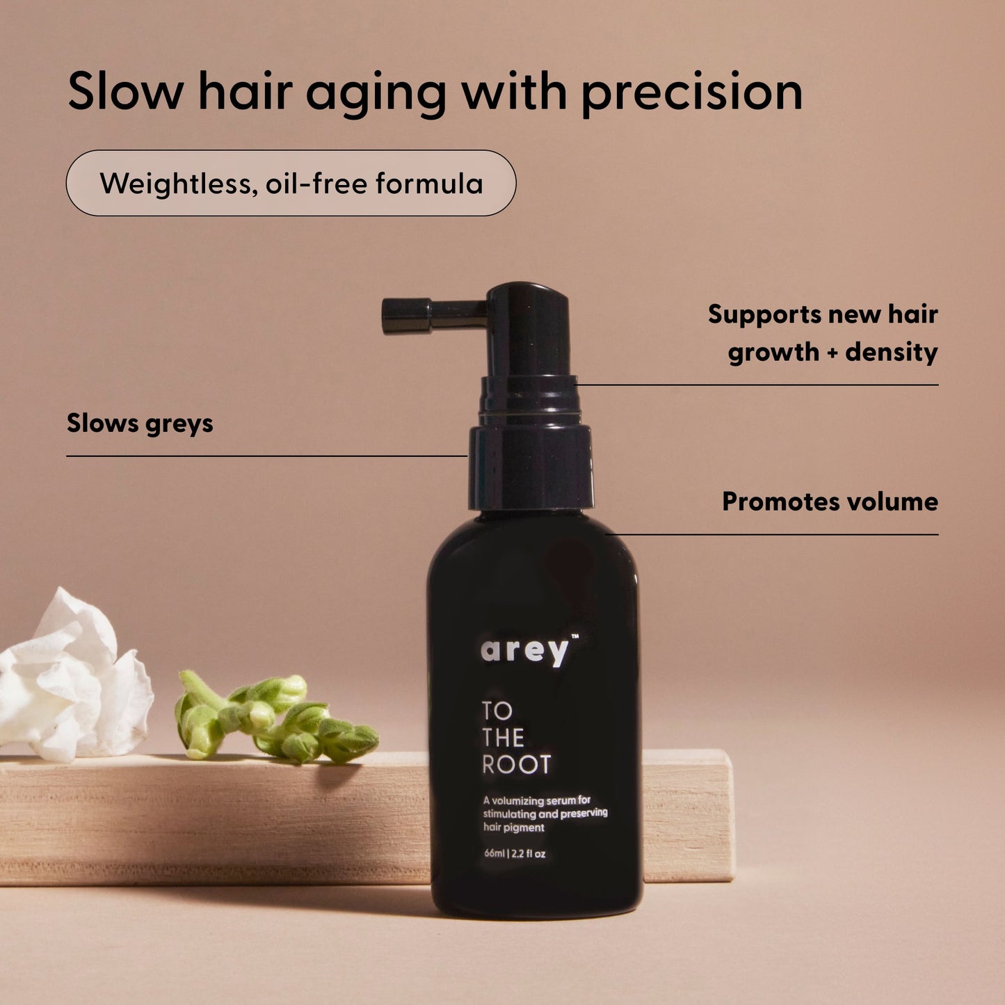 A black bottle of Arey’s To The Root® Scalp Serum rests on a wooden block alongside a flower and green buds, with surrounding text showcasing its benefits for slowing greys, repigmenting aging hair, promoting volume, and supporting hair growth.