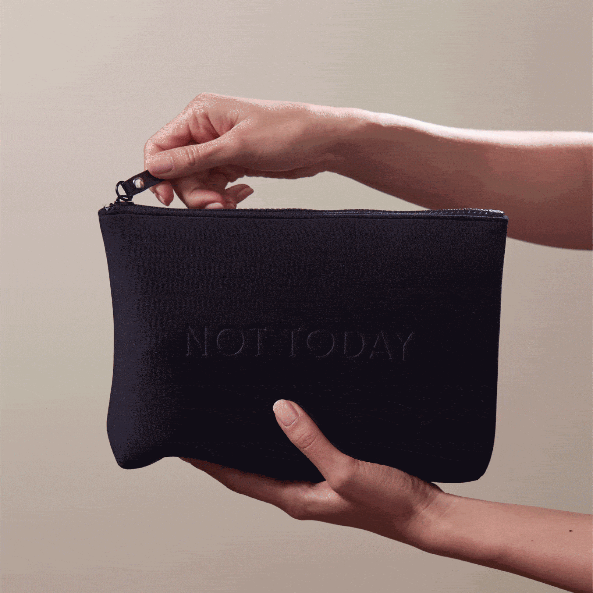 Animated GIF of hands holding the Arey "Not Today" black travel bag. The zippered pouch has "NOT TODAY" embossed on the front.