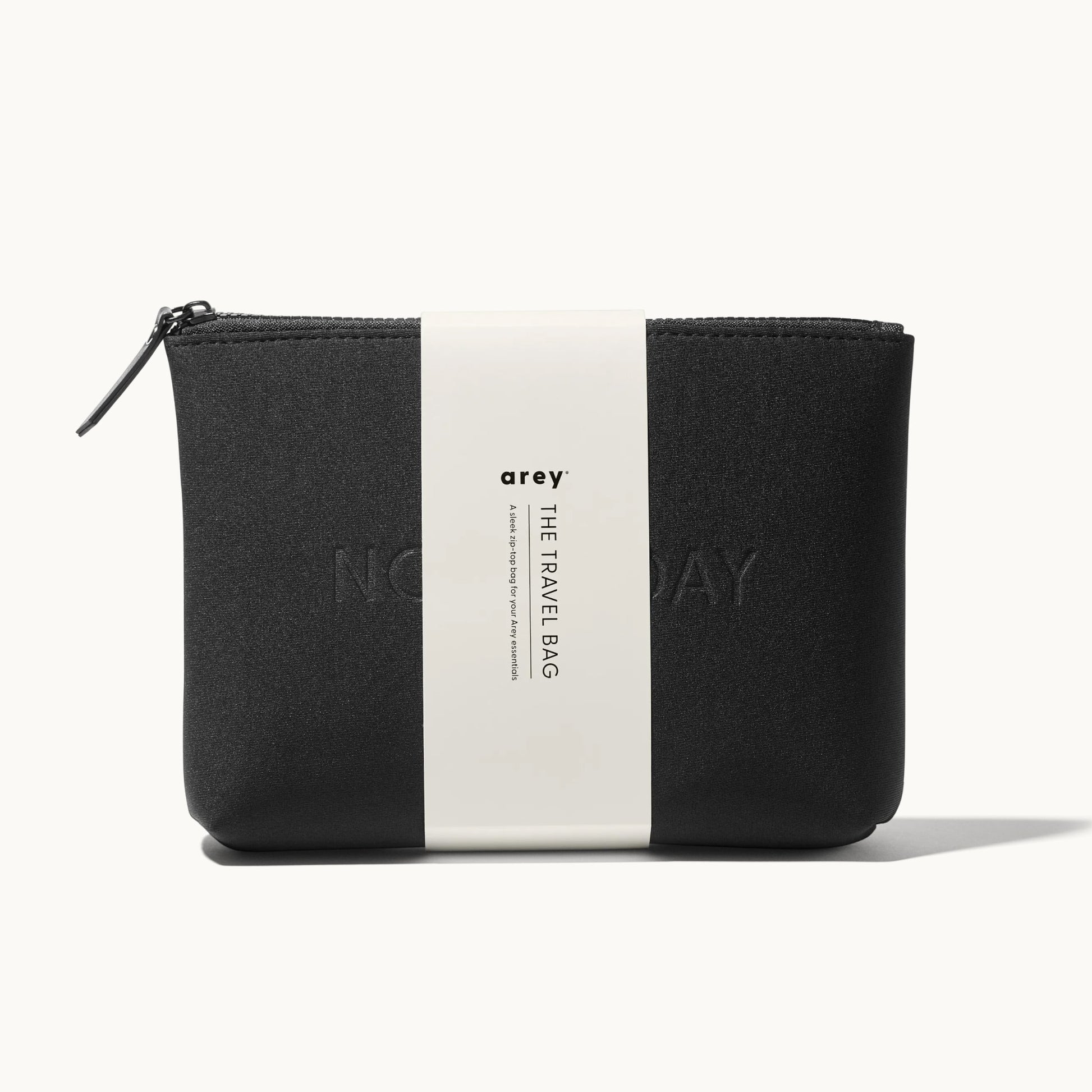 Arey "Not Today" black travel bag with a white paper band wrapped around it. The band reads: arey. THE TRAVEL BAG. A sleek zip-top bag for your Arey essentials.