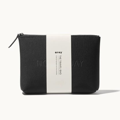 Arey "Not Today" black travel bag with a white paper band wrapped around it. The band reads: arey. THE TRAVEL BAG. A sleek zip-top bag for your Arey essentials.
