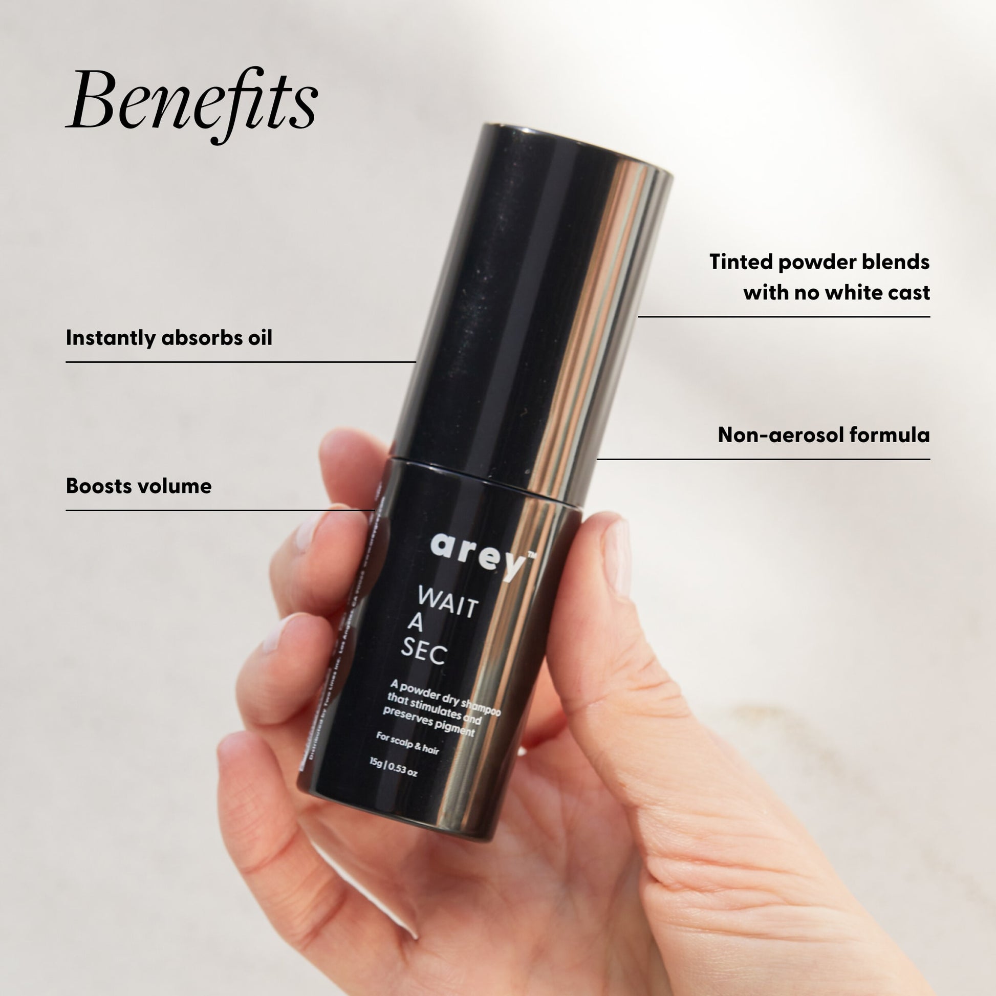 Hand holding a black cosmetic bottle labeled 'arey' with product benefits listed on a light gray background.