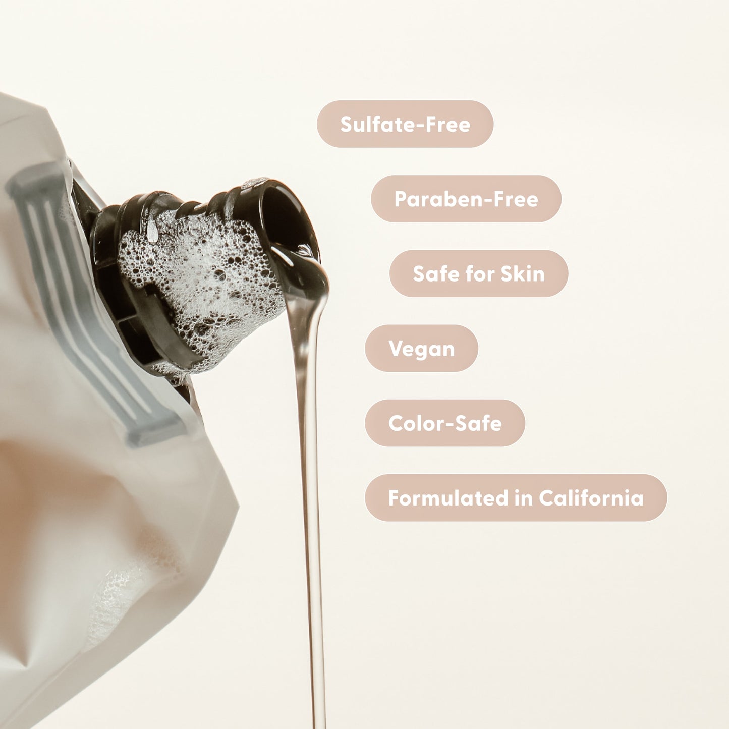 A pouch of Arey Wash Shampoo Refill pours liquid, with text bubbles highlighting its features: Sulfate-Free, Paraben-Free, Safe for Skin, Vegan, Color-Safe, and Formulated in California. This clean shampoo refill is specially designed to support hair health and delay greys, standing out against a neutral background.